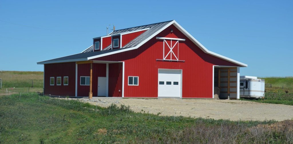 A bright red equestrian post-frame barn with an overhead door