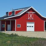 A bright red equestrian post-frame barn with an overhead door