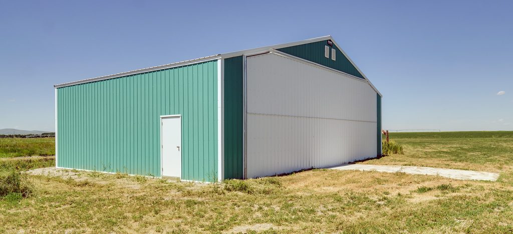 A turquoise post-frame airplane hangar with a bi-fold door