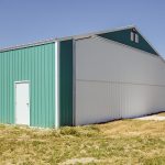 A turquoise post-frame airplane hangar with a bi-fold door