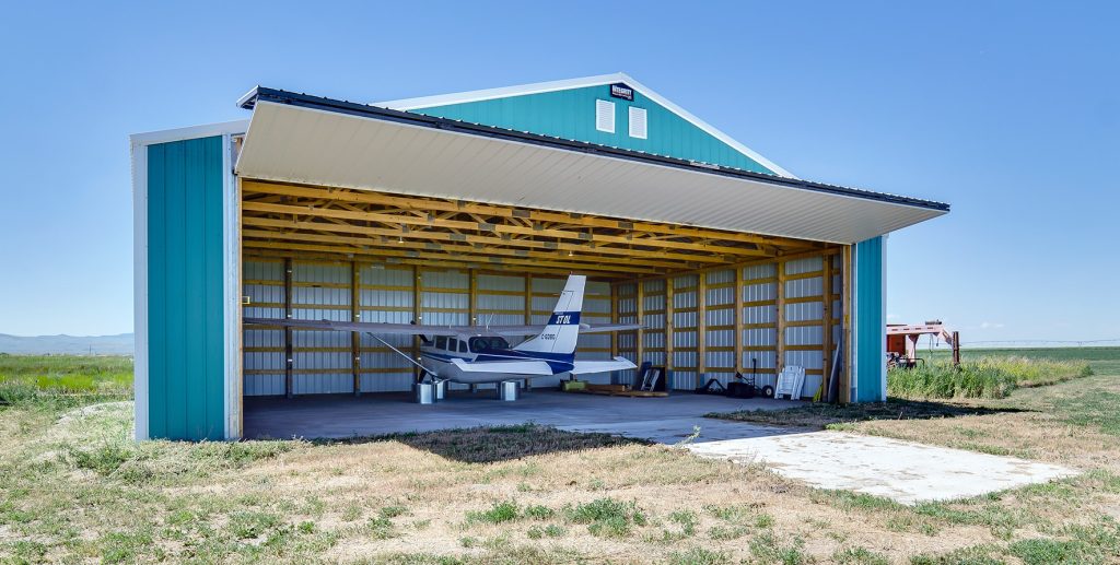 A turquoise post-frame airplane hangar with a bi-fold door