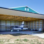 A turquoise post-frame airplane hangar with a bi-fold door