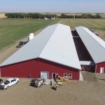 A dark red post-frame equestrian barn with four overhead and four bi-fold doors