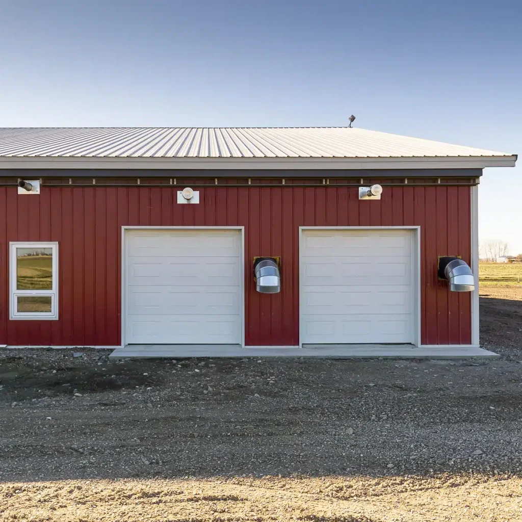 A dark red post-frame equestrian barn with four overhead and four bi-fold doors