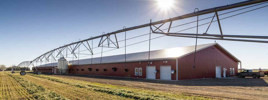 A dark red post-frame equestrian barn with four overhead and four bi-fold doors