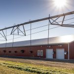 A dark red post-frame equestrian barn with four overhead and four bi-fold doors