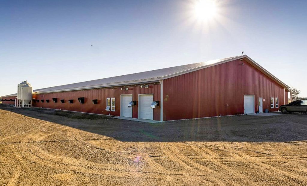 A dark red post-frame equestrian barn with four overhead and four bi-fold doors