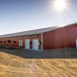 A dark red post-frame equestrian barn with four overhead and four bi-fold doors