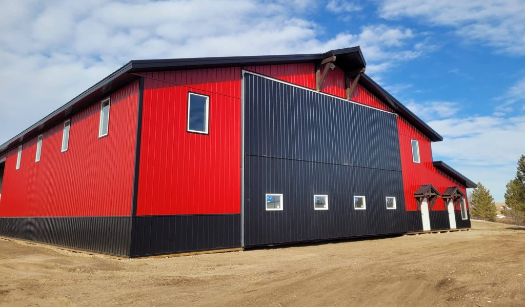 A dark red agricultural post-frame shop with two overhead doors, timber accents, crows peak, and a bi-fold door