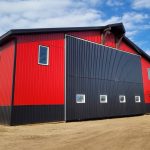 A dark red agricultural post-frame shop with two overhead doors, timber accents, crows peak, and a bi-fold door