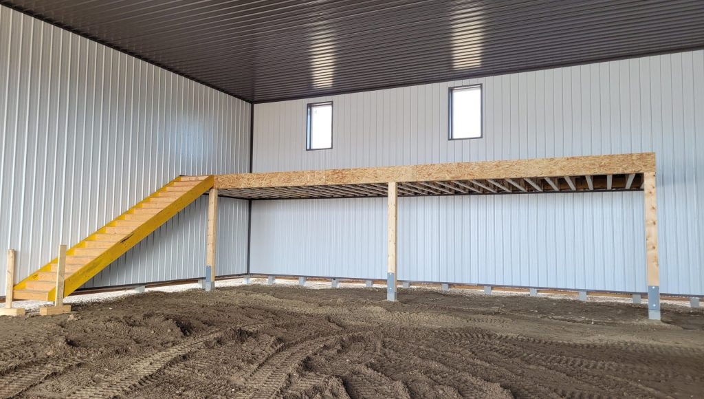 A dark red agricultural post-frame shop with two overhead doors, timber accents, crows peak, and a bi-fold door