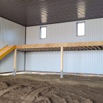 A dark red agricultural post-frame shop with two overhead doors, timber accents, crows peak, and a bi-fold door