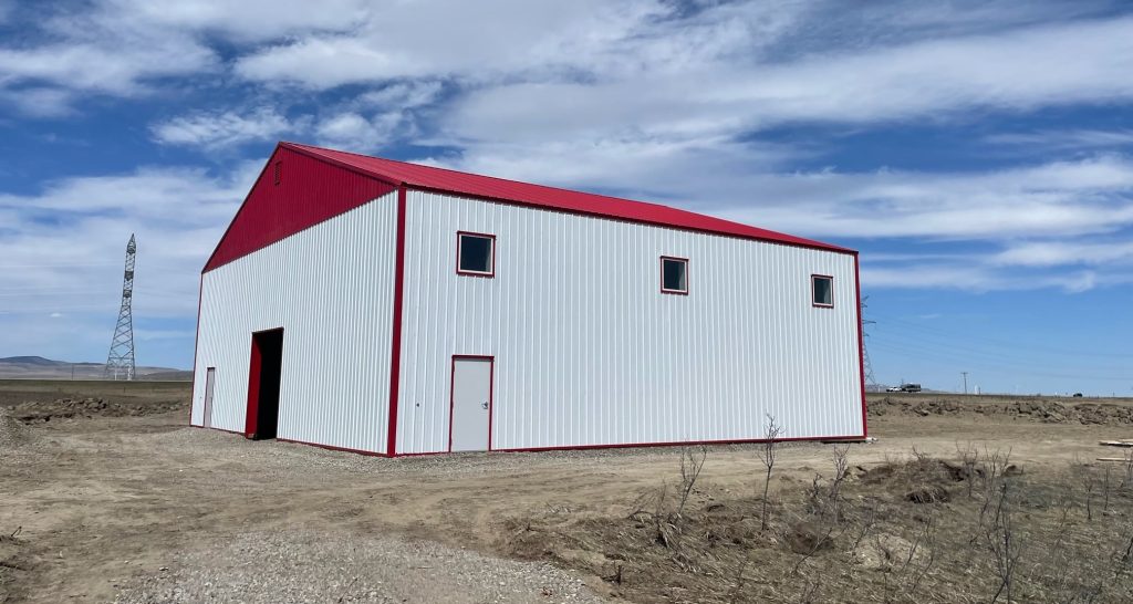 A bright white post-frame airplane hangar with a bright red bi-fold door and roof