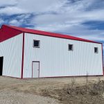A bright white post-frame airplane hangar with a bright red bi-fold door and roof