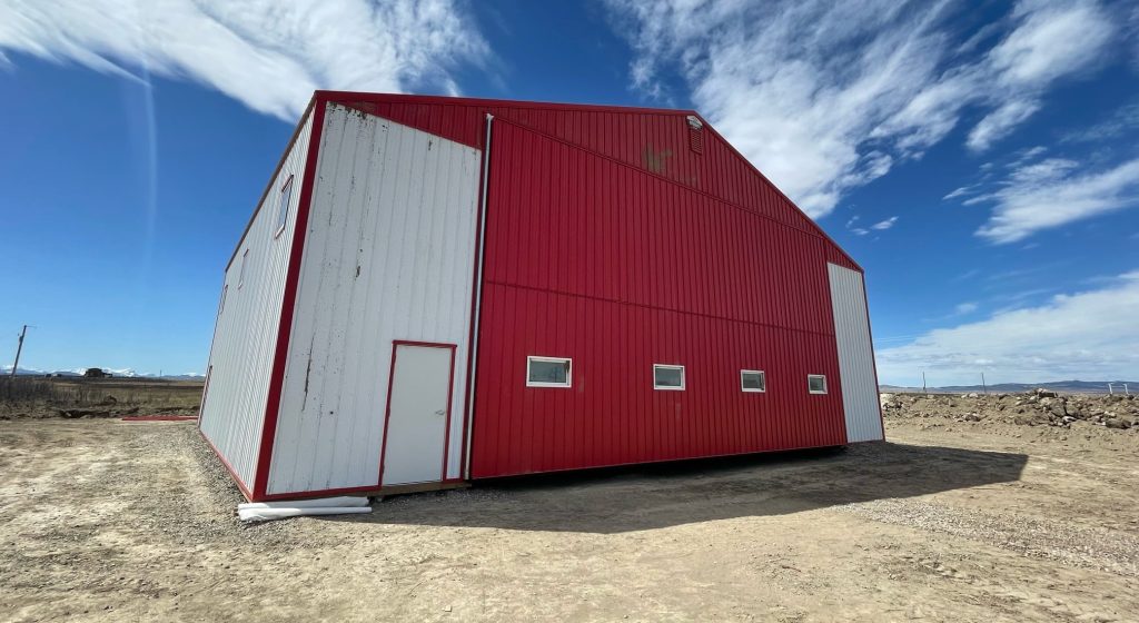 A bright white post-frame airplane hangar with a bright red bi-fold door and roof