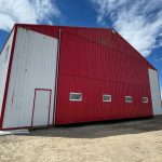 A bright white post-frame airplane hangar with a bright red bi-fold door and roof