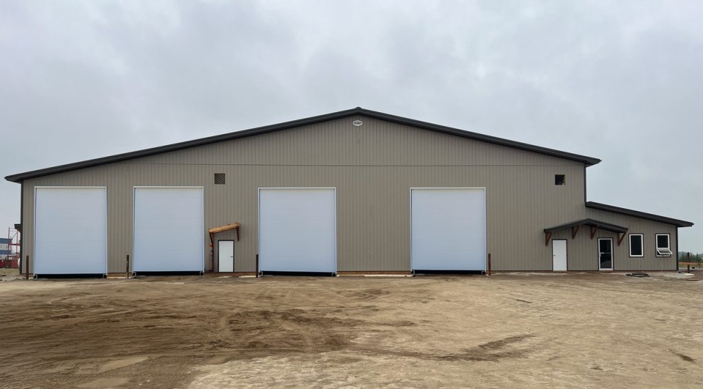 A hickory post-frame airplane hangar with 5 overhead doors and a bi-fold door