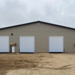 A hickory post-frame airplane hangar with 5 overhead doors and a bi-fold door