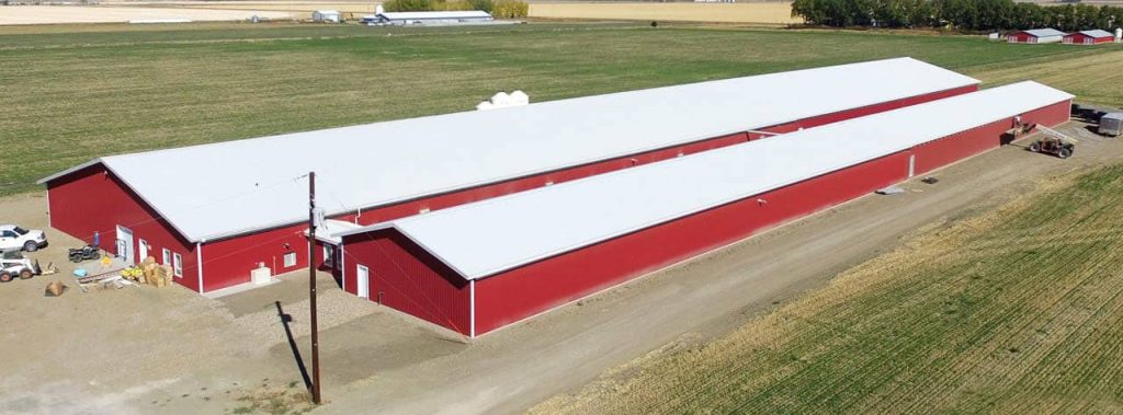A dark red post-frame equestrian barn with four overhead and four bi-fold doors