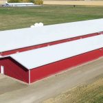 A dark red post-frame equestrian barn with four overhead and four bi-fold doors