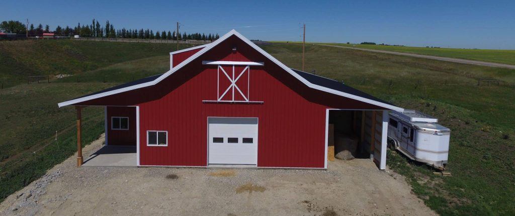 A bright red equestrian post-frame barn with an overhead door