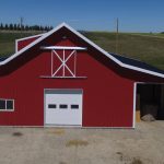 A bright red equestrian post-frame barn with an overhead door