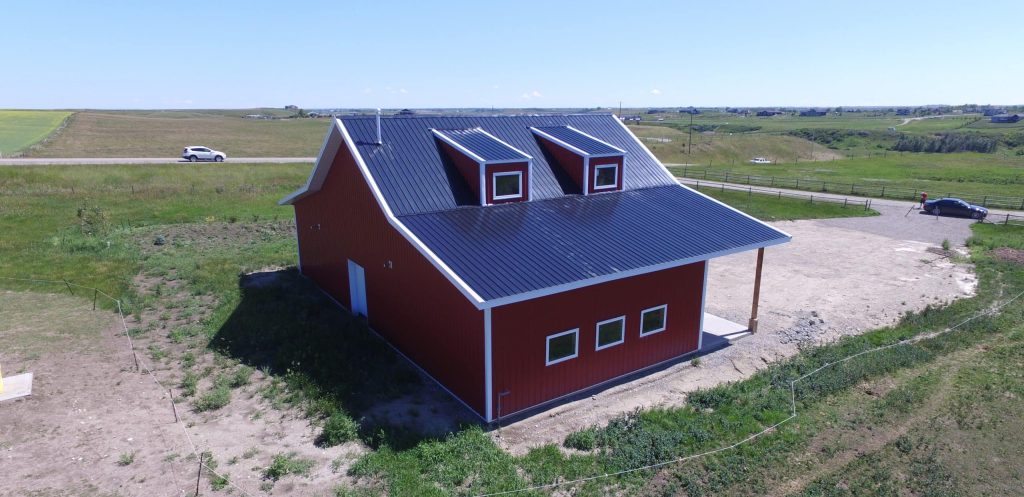 A bright red equestrian post-frame barn with an overhead door
