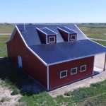 A bright red equestrian post-frame barn with an overhead door