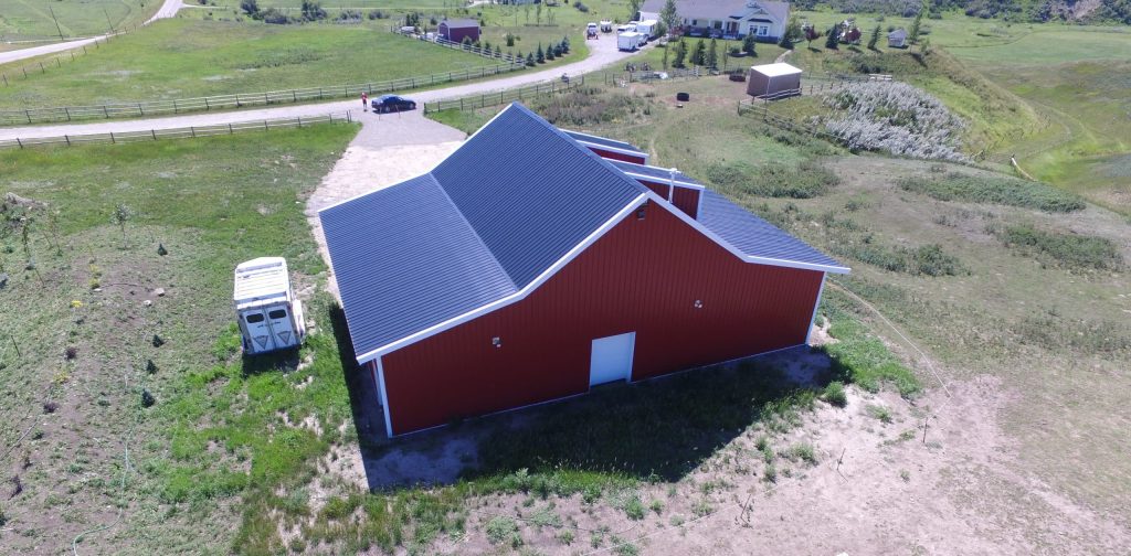 A bright red equestrian post-frame barn with an overhead door