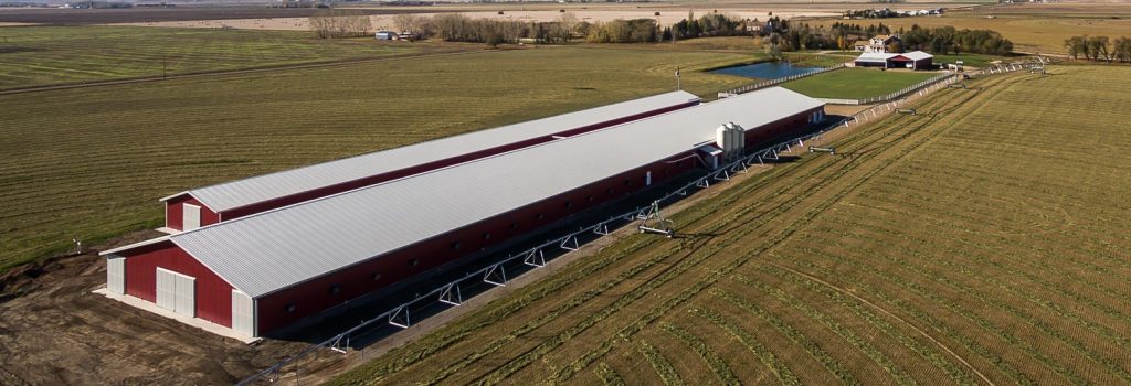 A dark red post-frame equestrian barn with four overhead and four bi-fold doors