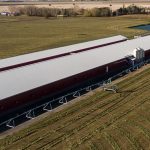 A dark red post-frame equestrian barn with four overhead and four bi-fold doors