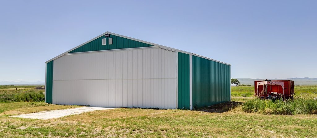 A turquoise post-frame airplane hangar with a bi-fold door