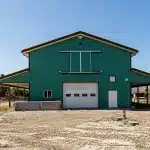 A turquoise post-frame equestrian barn