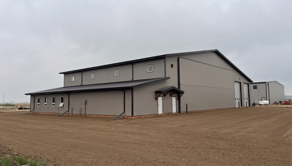 A hickory post-frame airplane hangar with 5 overhead doors and a bi-fold door