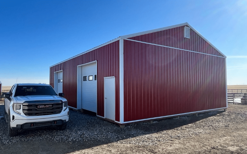 A dark red agricultural post-frame shop with two overhead doors