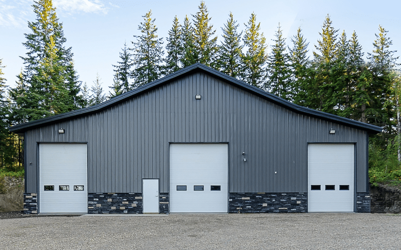 A charcoal agricultural post-frame shop with three overhead doors and wainscotting