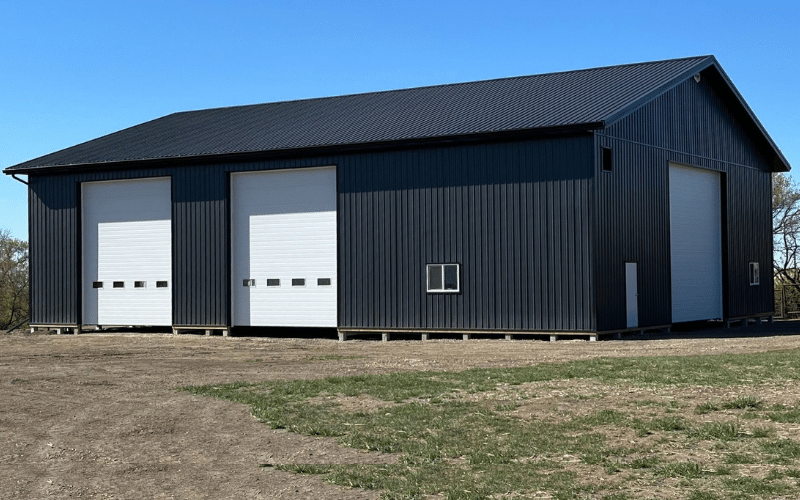 A black agricultural post-frame shop with three overhead doors