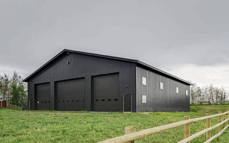 A black agricultural post-frame shop with three overhead doors
