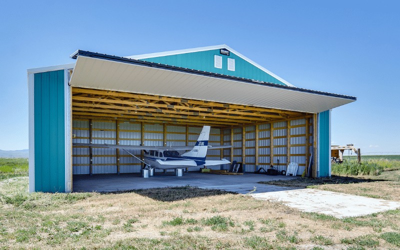 A turquoise post-frame airplane hangar with a bi-fold door