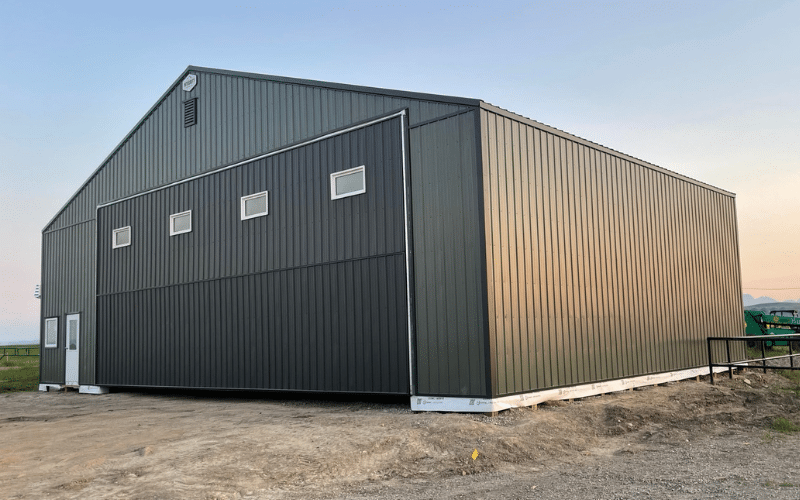 A dark sage post-frame airplane hangar with a bi-fold door