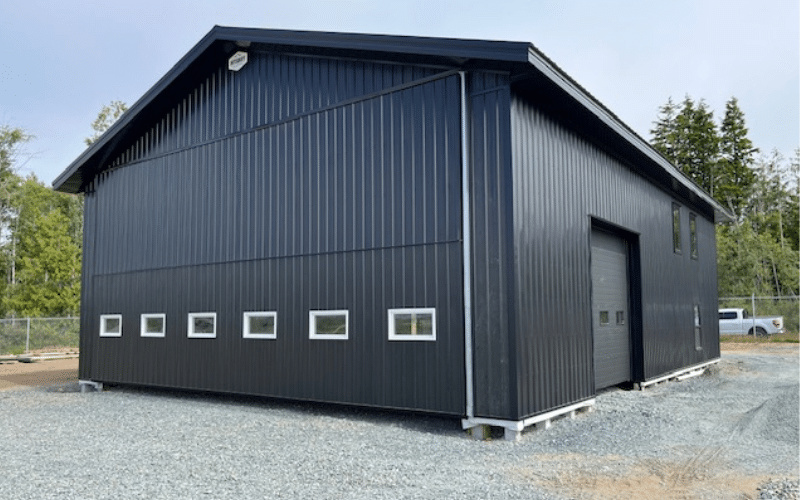 A black post-frame airplane hangar with a n overhead and bi-fold door