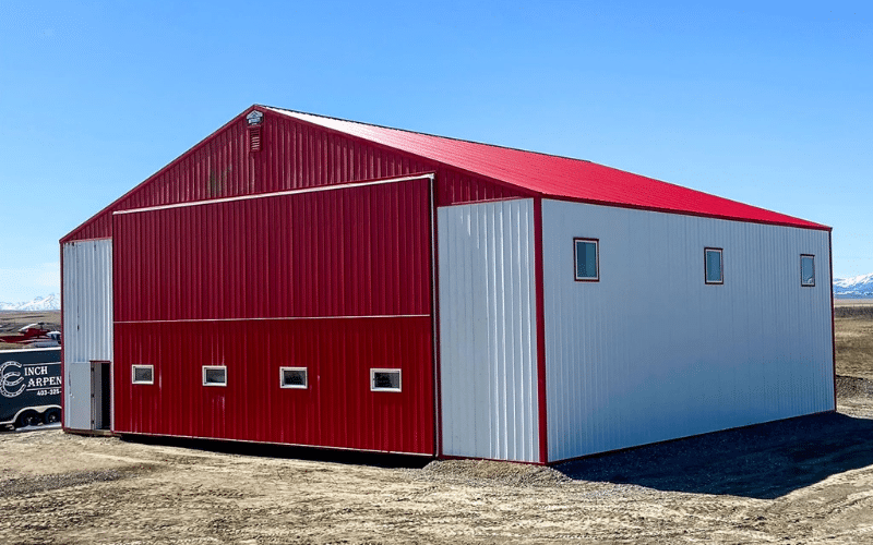 A bright white post-frame airplane hangar with a bright red bi-fold door and roof