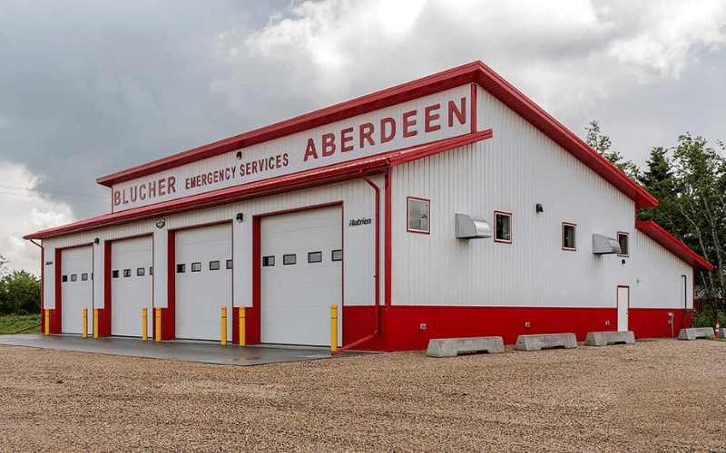 A bright white post-frame commercial building with four overhead doors