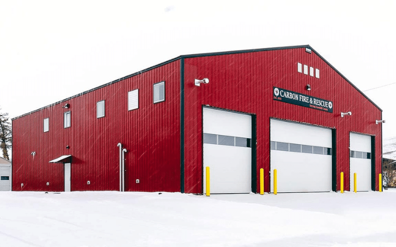 A dark red post-frame commercial build with four overhead doors