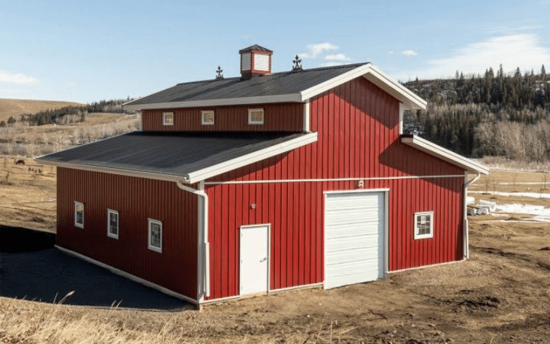 A dark red post-frame equestrian barn with two overhead doors