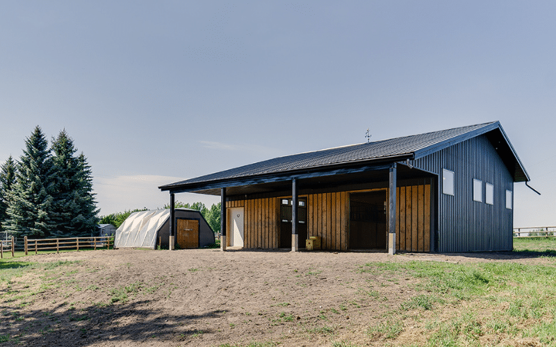 A charcoal post-frame equestrian barn with three overhead doors