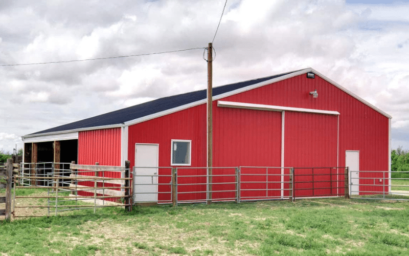 A bright red post-frame equestrian barn with six sliding doors