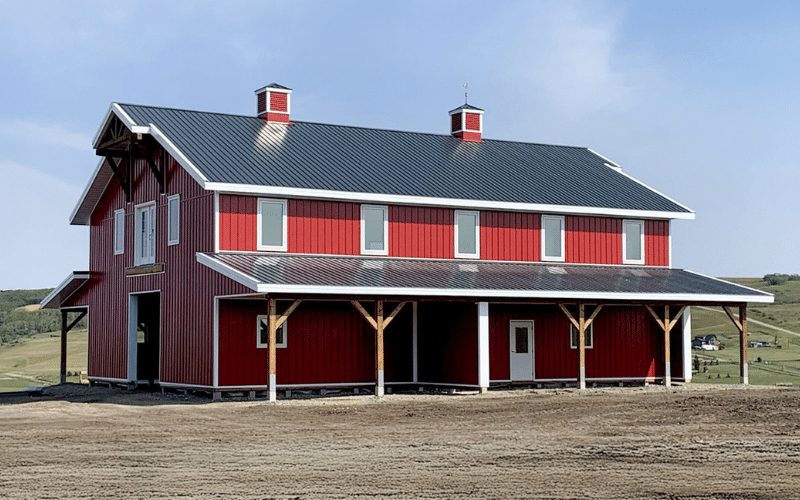 A dark red post-frame equestrian barn with two overhead doors