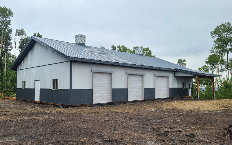 A bone white post-frame equestrian barn with four overhead doors