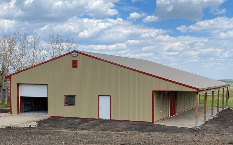 A tan post-frame equestrian barn with two overhead and two sliding doors